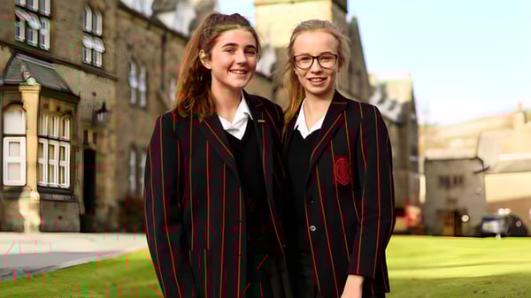 Zwei Schülerinnen der Giggleswick School stehen im Campusbereich nebeneinander und tragen Hogwarts-Stil Uniformen.