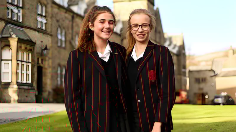 Zwei Schülerinnen der Giggleswick School stehen im Campusbereich nebeneinander und tragen Hogwarts-Stil Uniformen.