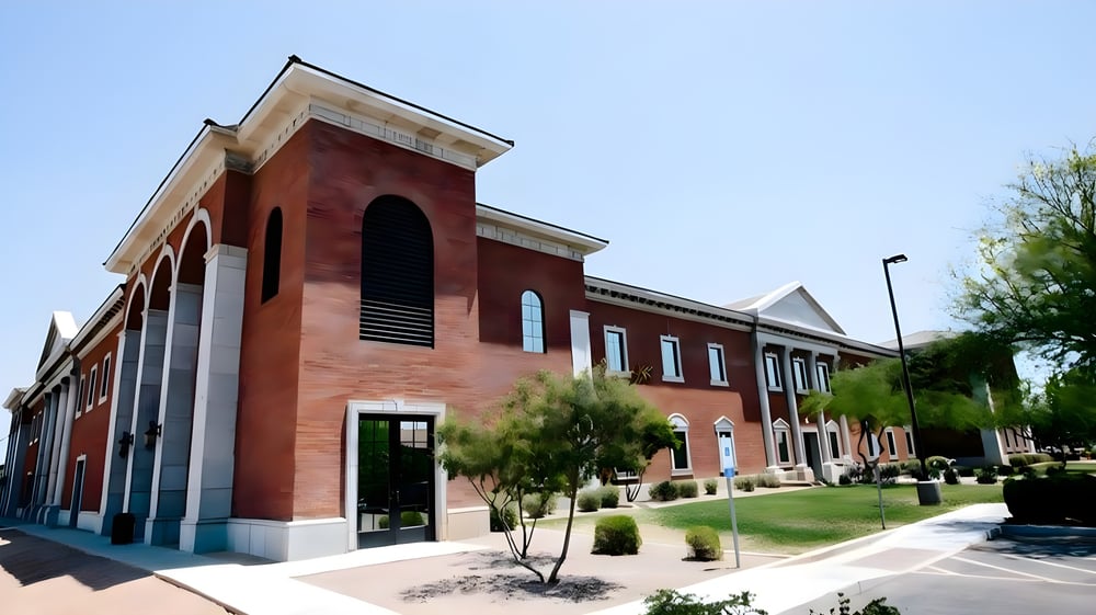 Das große Backsteingebäude mit Bögen und Eingang auf dem Campus der Gilbert Christian Schools ist von gepflegter Landschaft mit Bäumen umgeben.