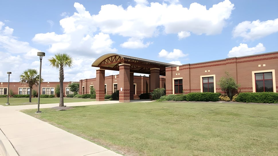 Ein Backsteingebäude mit einem bogenförmigen Eingang steht auf einer Rasenfläche mit Palmen auf dem Gelände der Gilbert Public Schools.
