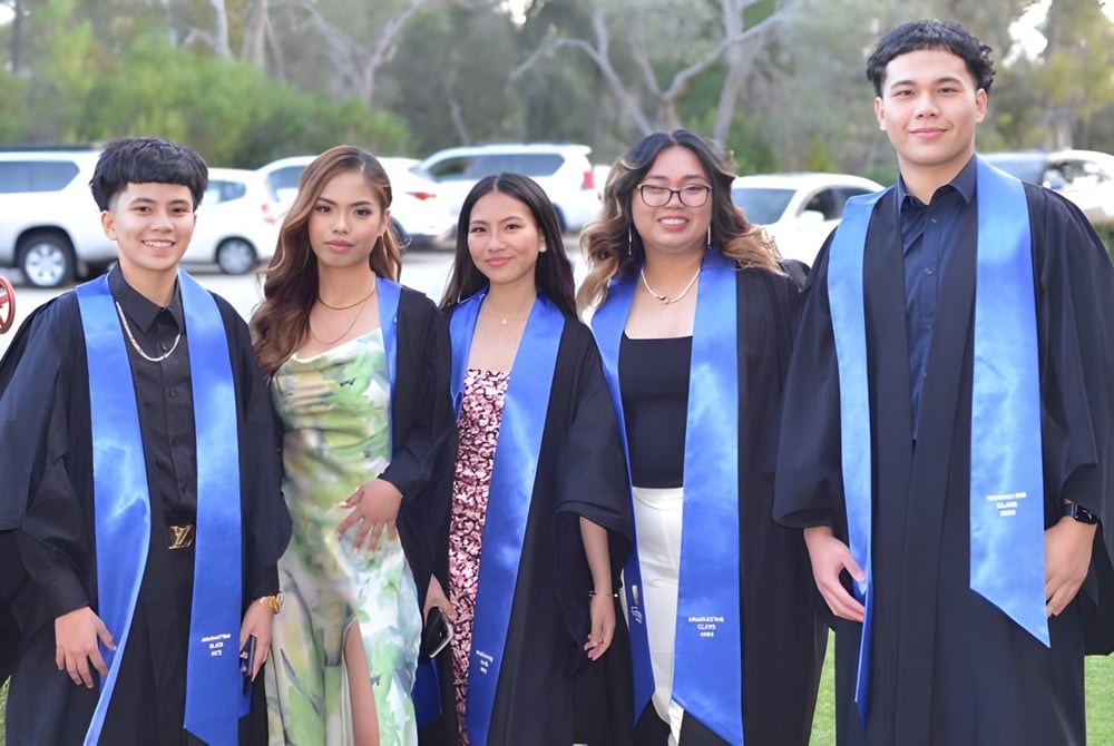Eine Gruppe von fünf Absolventen steht im Freien auf dem Campus des Gilmore College in ihren Abschlussroben.
