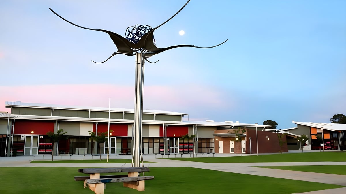 Eine große Metallskulptur in Form eines Schmetterlings steht auf einem hohen Pfahl vor dem modernen Gebäudekomplex des Gilmore College.