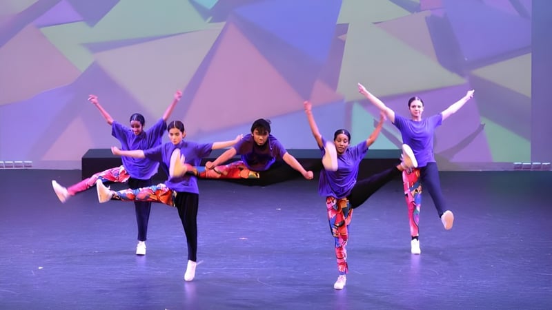 Eine Gruppe von Schülern der Girrawheen Senior High School tanzt auf der Bühne vor einem Hintergrund aus violetten und blauen geometrischen Formen.