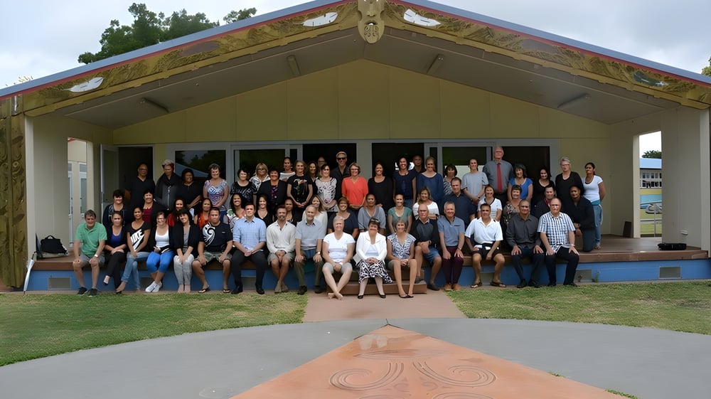 Eine Gruppe aus Schülerinnen, Schülern und Erwachsenen steht vor dem farbenfrohen Gebäude der Gisborne Girls' High School.