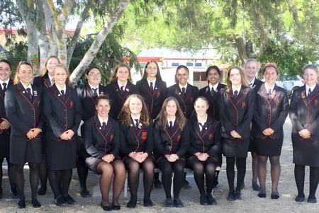 Eine Gruppe von Schülerinnen der Gisborne Girls' High School posiert gemeinsam draußen inmitten grüner Bäume.