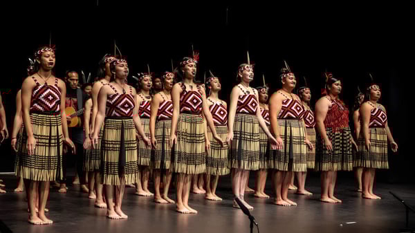 Eine Gruppe von Schülerinnen der Gisborne Girls' High School steht auf der Bühne in traditionellen tribal-inspirierten Kostümen mit aufwendigen Mustern.