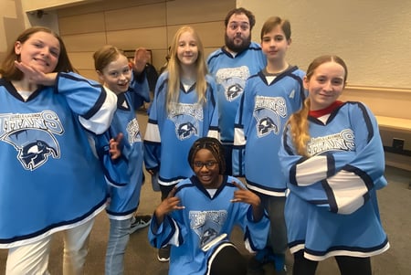 Eine Gruppe von Schülerinnen und Schülern der École secondaire publique Gisèle-Lalonde trägt blaue Trikots und posiert gemeinsam in der Umkleidekabine.