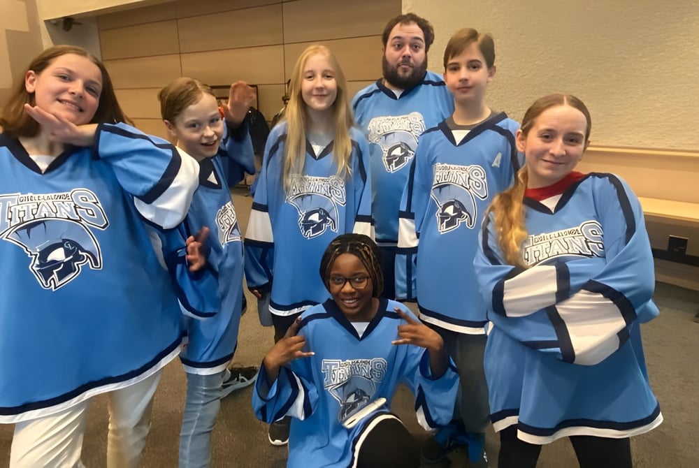 Eine Gruppe von Schülerinnen und Schülern der École secondaire publique Gisèle-Lalonde trägt blaue Trikots und posiert gemeinsam in der Umkleidekabine.