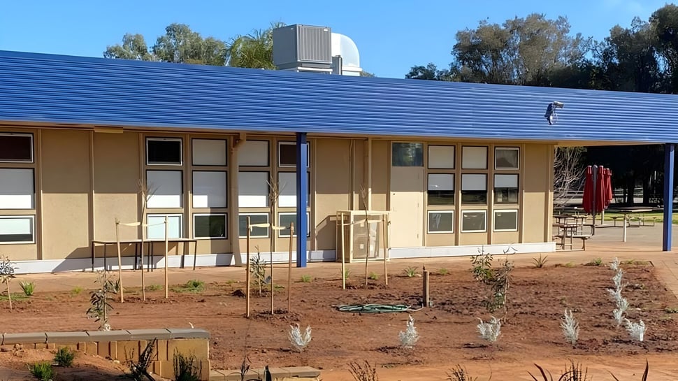 Das einstöckige Gebäude der Gladstone High School steht in einer Wüstenlandschaft umgeben von kleinen Pflanzen und Bäumen.