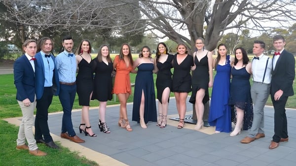 Eine Gruppe von Personen steht zusammen im Freien auf dem Gelände der Gladstone High School vor Bäumen und Grünflächen.