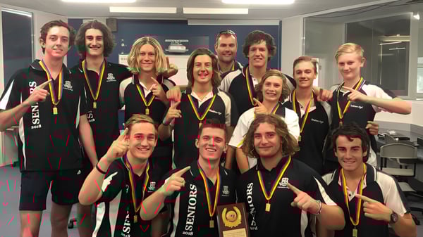 Eine Gruppe von Schülerinnen und Schülern der Gladstone High School posiert in der Umkleide mit Medaillen und Trophäen.