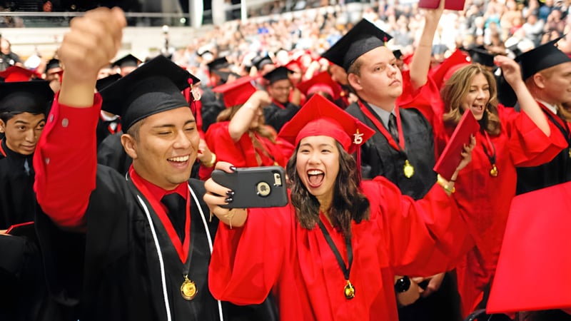 Eine große Gruppe von Absolventinnen und Absolventen der Gladstone Secondary School feiert in roten Talaren ihren Abschluss und macht Selfies.