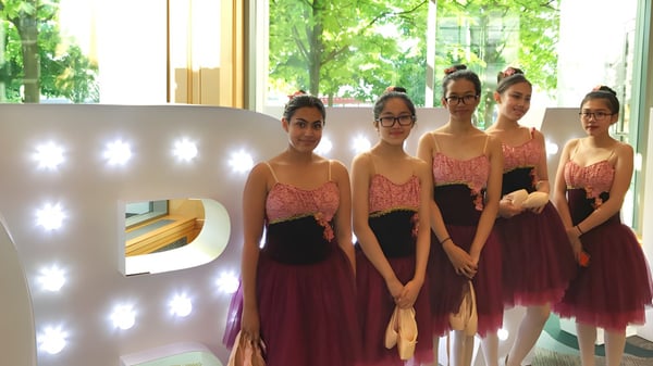 Eine Gruppe junger Frauen in eleganten Kleidern steht vor einem großen beleuchteten Buchstaben P auf dem Campus der Gladstone Secondary School.