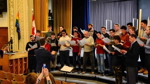 Ein Chor des Glebe Collegiate Institute tritt auf einer Bühne mit dekorativen Elementen und Flaggen im Hintergrund auf.