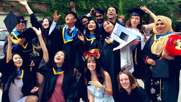 Eine Gruppe von Absolventinnen und Absolventen in farbenfrohen Talaren feiert vor einem Backsteingebäude auf dem Gelände des Glebe Collegiate Institute.