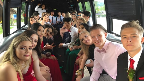 Eine Gruppe von Schülerinnen und Schülern der Gleneagle Secondary School in formeller Kleidung sitzt gemeinsam in einem Bus im Freien.