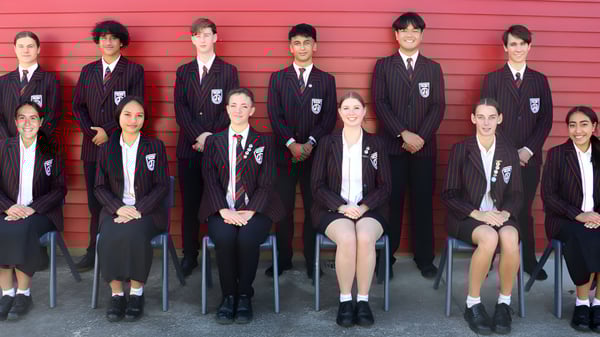 Eine Gruppe Schülerinnen und Schüler des Glenfield College steht vor einer roten Holzwand.