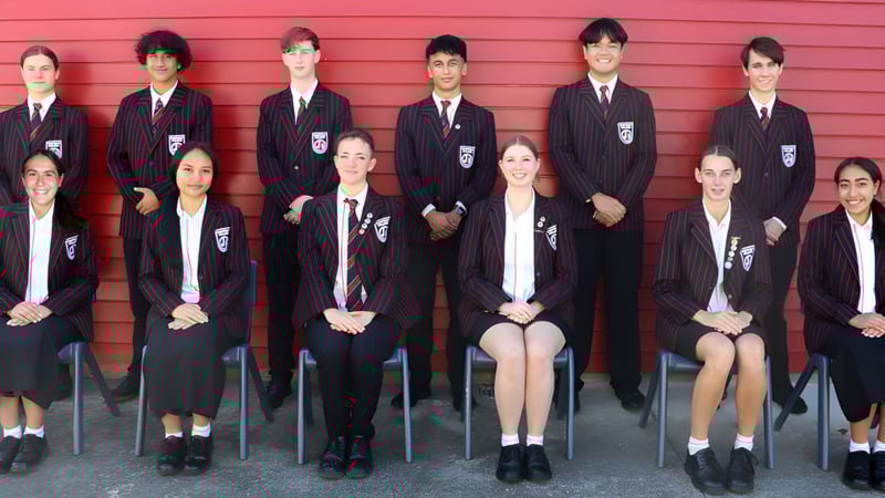 Eine Gruppe Schülerinnen und Schüler des Glenfield College steht vor einer roten Holzwand.