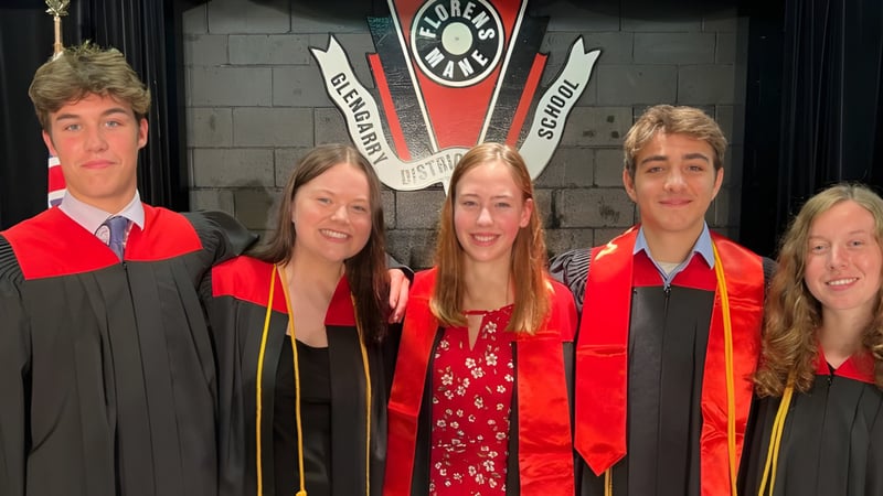Fünf Schülerinnen und Schüler der Glengarry District High School stehen in Abschlusskleidung vor einem Universitätswappen.