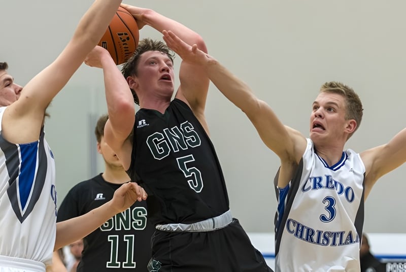 Drei Schülerinnen und Schüler der Glenlyon Norfolk School kämpfen um den Ball auf dem Basketballfeld.