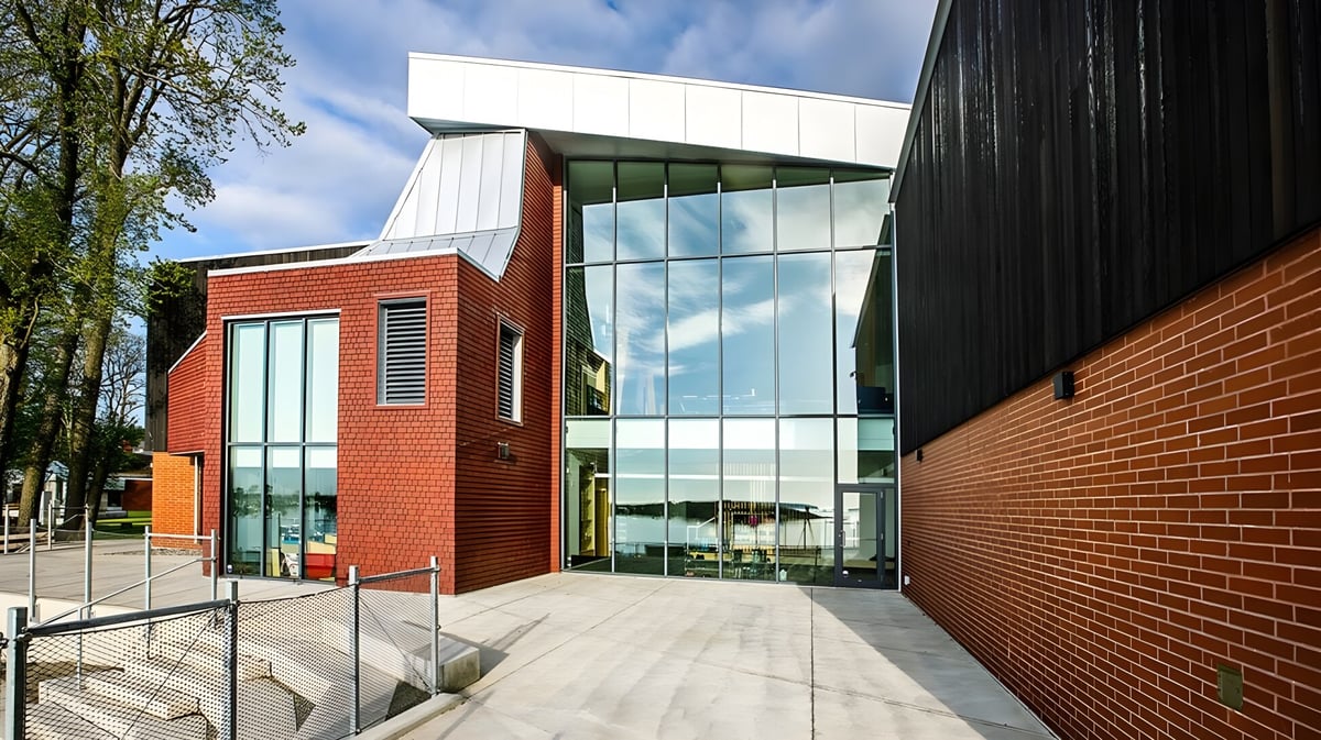 Das moderne mehrstöckige Gebäude der Glenlyon Norfolk School mit roten Backstein- und Glasfassaden ist von Bäumen umgeben.