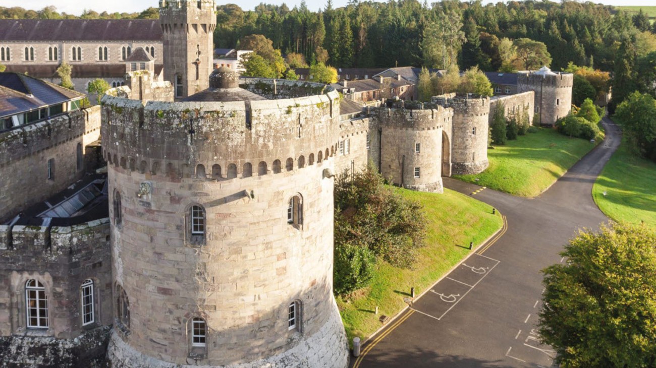 Das mittelalterliche Schloss der Glenstal Abbey School ist von grüner Landschaft und einer gewundenen Straße umgeben.