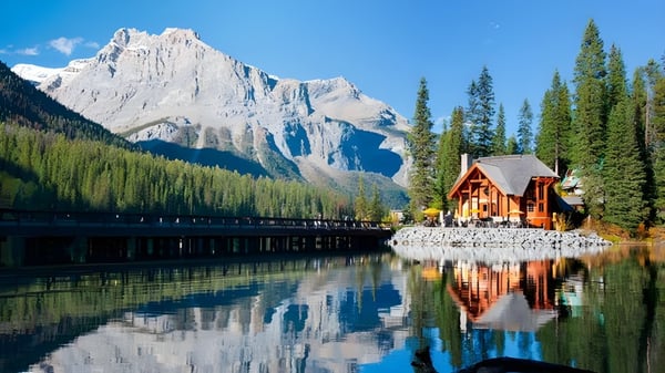 Eine malerische Berglandschaft mit See und Holzhaus spiegelt sich im ruhigen Wasser ohne Bezug zur Gloucester High School.
