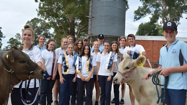 Eine Gruppe Schüler der Gloucester High School posiert mit Tieren vor einem großen Metallsilo in ländlicher Umgebung.