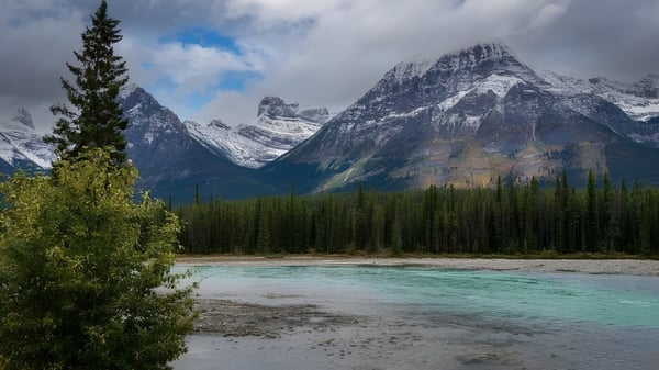 Eine ruhige Berglandschaft mit einem türkisfarbenen Fluss und schneebedeckten Gipfeln im Hintergrund.