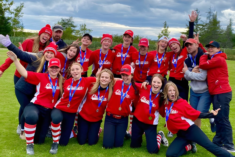 Schüler der Glovertown Academy feiern gemeinsam auf einer Wiese vor bewölktem Himmel.