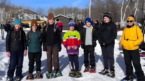 Eine Gruppe von Schülern der Glovertown Academy steht im Winter mit warmer Kleidung vor einem Holzgebäude im Schnee.