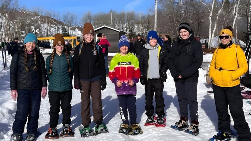 Eine Gruppe von Schülern der Glovertown Academy steht im Winter mit warmer Kleidung vor einem Holzgebäude im Schnee.