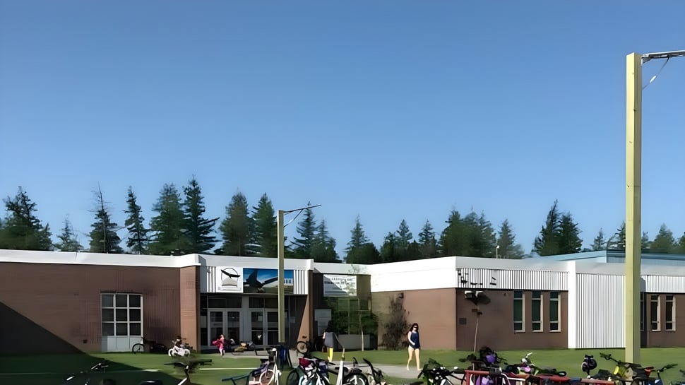 Das moderne Schulgebäude der Glovertown Academy mit Schülergruppen auf der Wiese davor und Wald im Hintergrund.