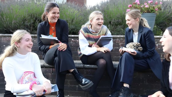 Vier Schülerinnen der Godolphin School sitzen auf einer Mauer und unterhalten sich in einer grünen Umgebung.