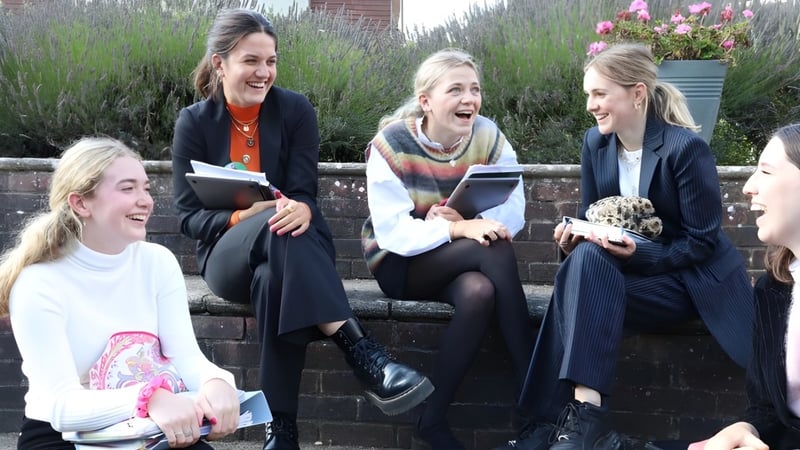 Vier Schülerinnen der Godolphin School sitzen auf einer Mauer und unterhalten sich in einer grünen Umgebung.