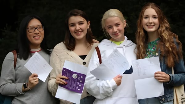 Vier Schülerinnen der Godolphin School halten lächelnd Papiere vor dunklem Hintergrund.