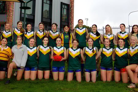 Eine Gruppe Schülerinnen der Golden Grove High School posiert im grünen und gelben Sporttrikot vor einem Backsteingebäude im Freien.