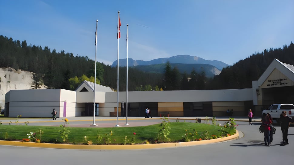 Das moderne mehrstöckige Gebäude der Golden Secondary School mit Flaggen auf dem Dach steht vor bewaldeten Bergen und gepflegtem Rasen.
