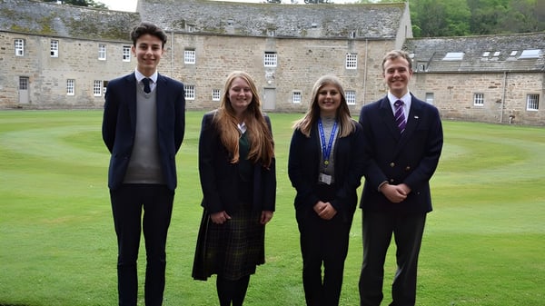 Vier Personen stehen gemeinsam im grasbewachsenen Innenhof der Gordonstoun School zwischen Steingebäuden.