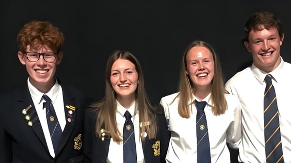 Vier Schülerinnen und Schüler in Schuluniform posieren lächelnd vor dunklem Hintergrund auf dem Campus der Gore High School.