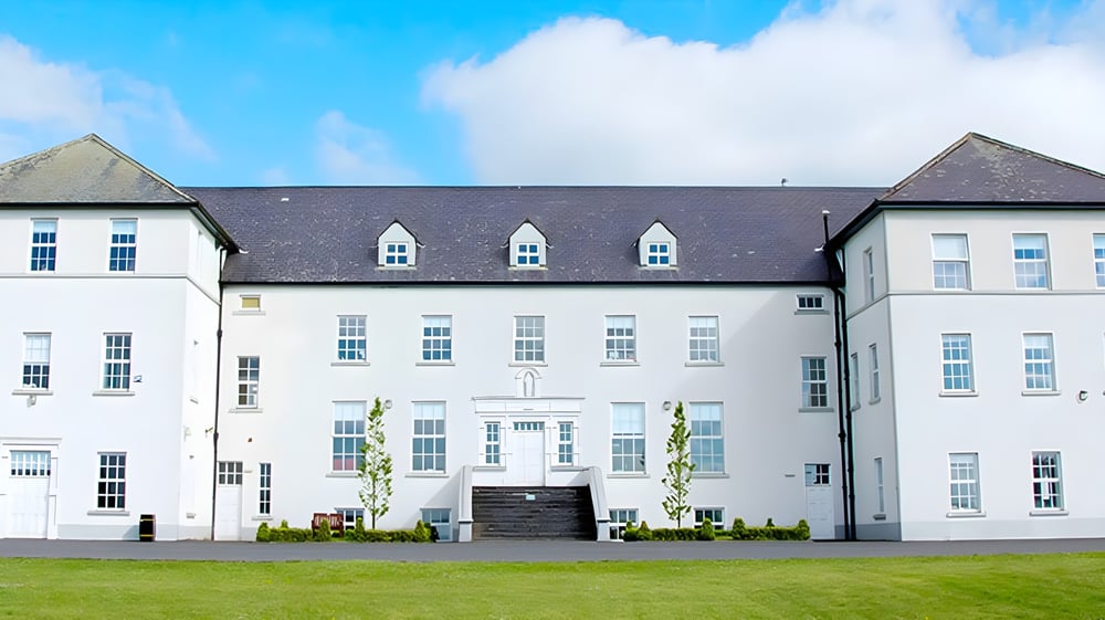Das weiße Gebäude mit Giebeldach und Gauben im Innenhof der Gortnor Abbey steht unter einem hellblauen Himmel.
