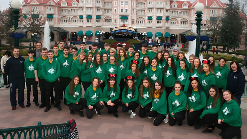 Eine Gruppe von Schülerinnen und Schülern der Gortnor Abbey trägt grüne Shirts vor einem bunten, schlossähnlichen Gebäude in einem Freizeitpark.