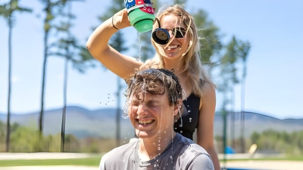Eine Frau sprüht spielerisch Wasser ins Gesicht eines Mannes auf dem Campus der Gould Academy im Freien.