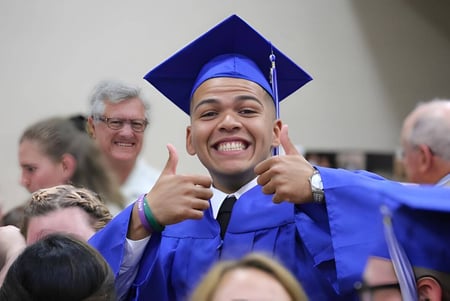 Ein Schüler der Grace Academy trägt eine blaue Abschlussrobe und zeigt beim Abschlussjubel ein Daumen-hoch-Geste.