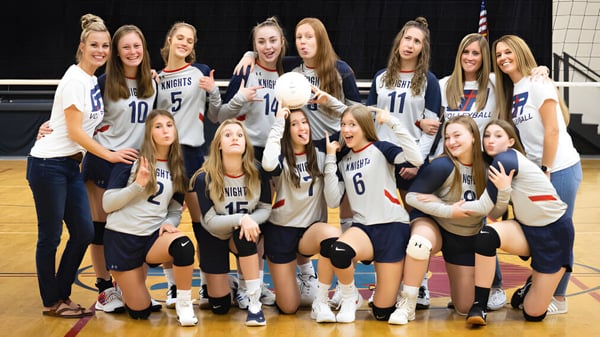 Eine Gruppe junger Volleyballspielerinnen der Grace Academy posiert gemeinsam auf einem Basketballfeld.