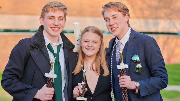 Drei Schüler der Grand Rapids Christian High School stehen draußen vor einem Holzzaun und Bäumen zusammen.