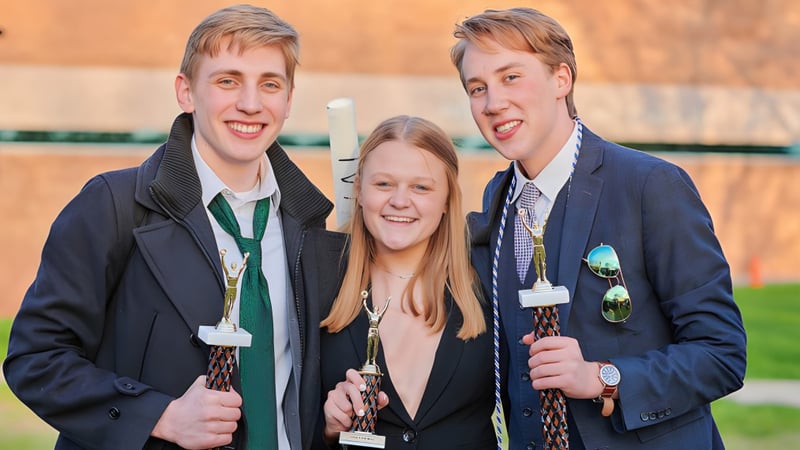 Drei Schüler der Grand Rapids Christian High School stehen draußen vor einem Holzzaun und Bäumen zusammen.