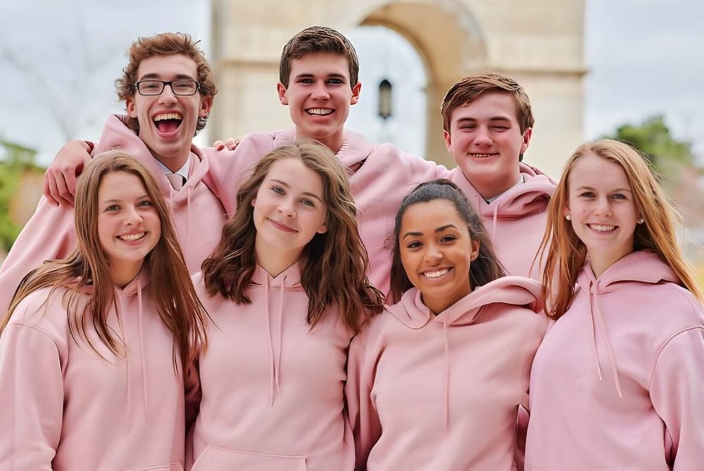 Eine Gruppe Schülerinnen und Schüler in pinken Hoodies steht gemeinsam vor einem Gebäude auf dem Campus der Grand Rapids Christian High School.
