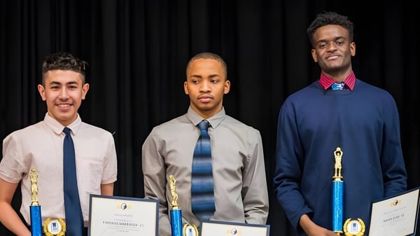 Drei junge Männer in formeller Kleidung halten Urkunden vor einem dunklen Vorhang auf der Grand River Academy.