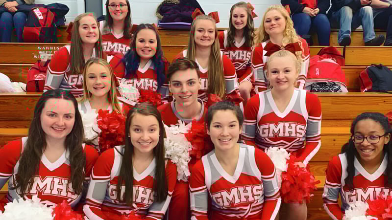 Eine Gruppe Cheerleader in roten und weißen Uniformen posiert mit Pompons in der Turnhalle der Grand River Academy.